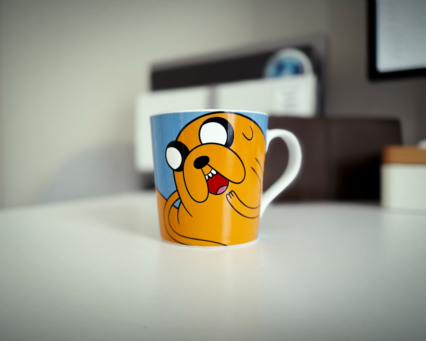 Photo of a coffee cup featuring Jake from Adventure Time. Background is softly focused. 